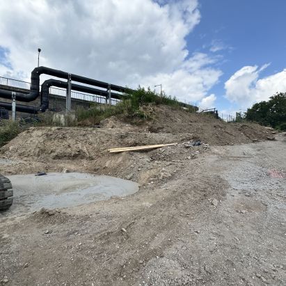 Bagger auf Baustelle mit Rohren im Hintergrund