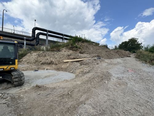 Bagger auf Baustelle mit Rohren im Hintergrund