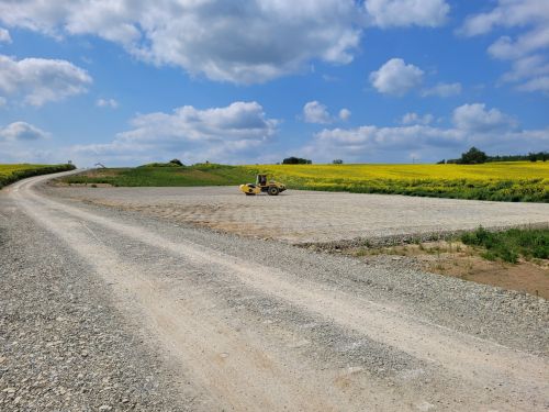 Feldstraße mit Bagger und Rapsfeld im Hintergrund