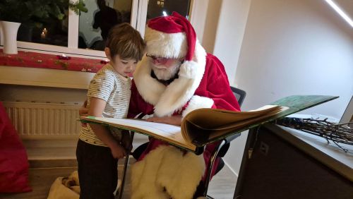 A man in a Santa Claus costume reading to a boy from a large book.